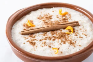 A bowl of creamy sweet rice garnished with almonds, mango, and cinnamon.