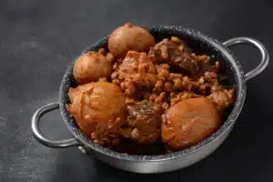 Traditional haminé in a bowl with beef, chickpeas, potatoes, and egg garnished with parsley.