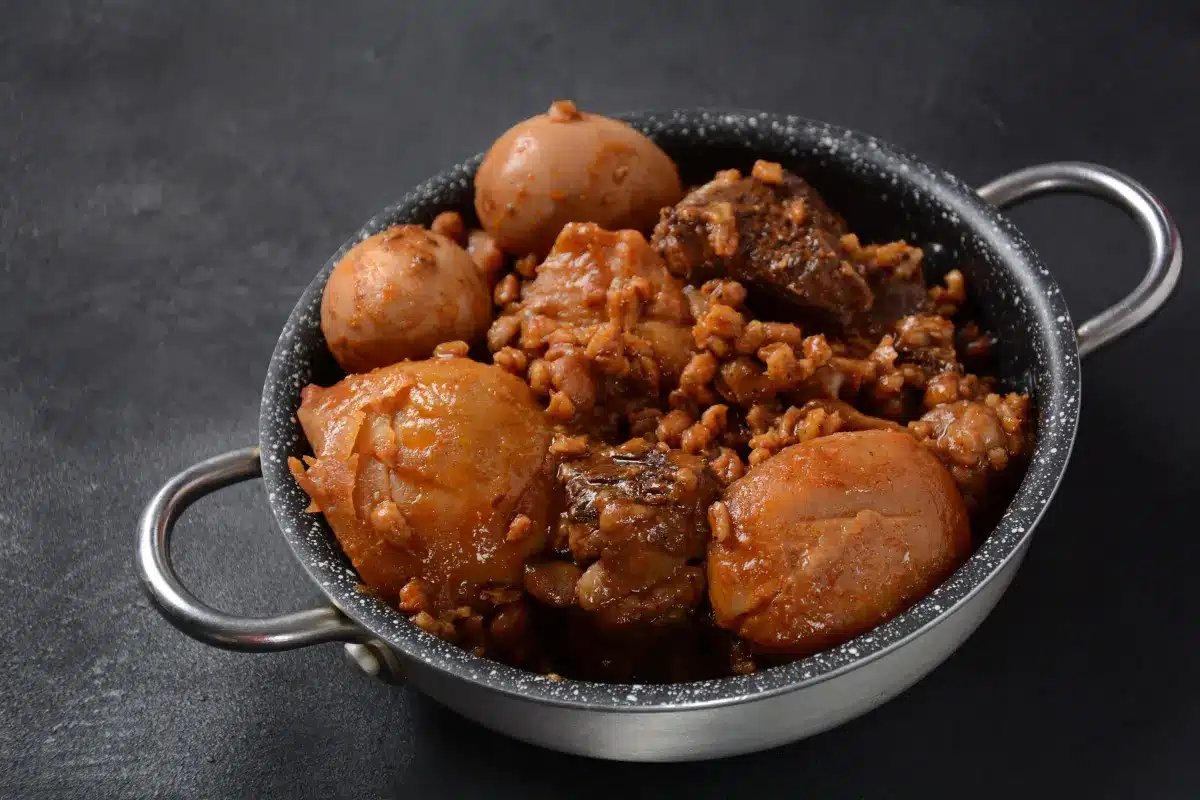 Traditional haminé in a bowl with beef, chickpeas, potatoes, and egg garnished with parsley.