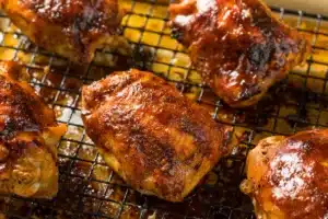 Smoked chicken thigh on a wooden board with fresh herbs and BBQ sauce in the background.