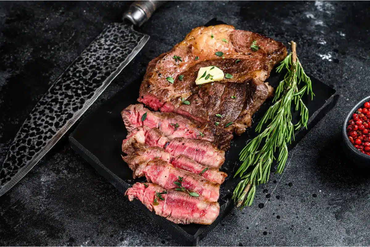 A cooked chuck steak with herb butter on a wooden board.