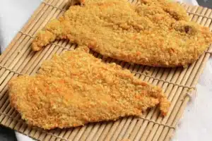 Golden crispy chicken cutlets on a plate with parsley and lemon.