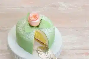 Elegant Princess Cake with green marzipan, raspberry jam, and custard layers, adorned with a pink marzipan rose.