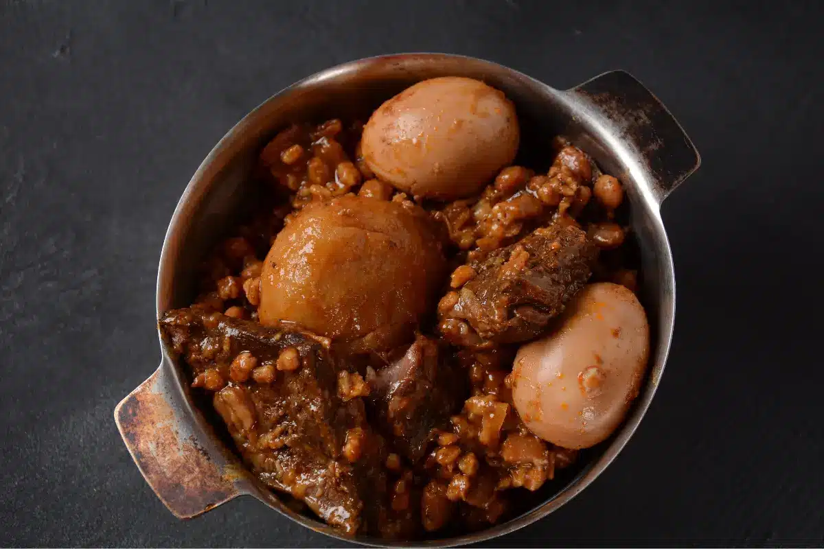 Traditional haminé in a bowl with beef, chickpeas, potatoes, and egg garnished with parsley.