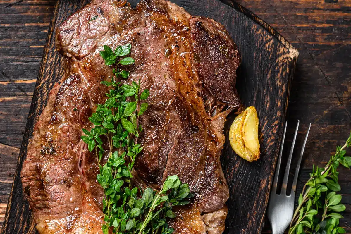 A cooked chuck steak with herb butter on a wooden board.