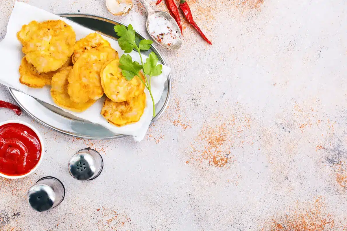 Crispy chicken cutlets with sides of green beans and mashed potatoes on a wooden table.