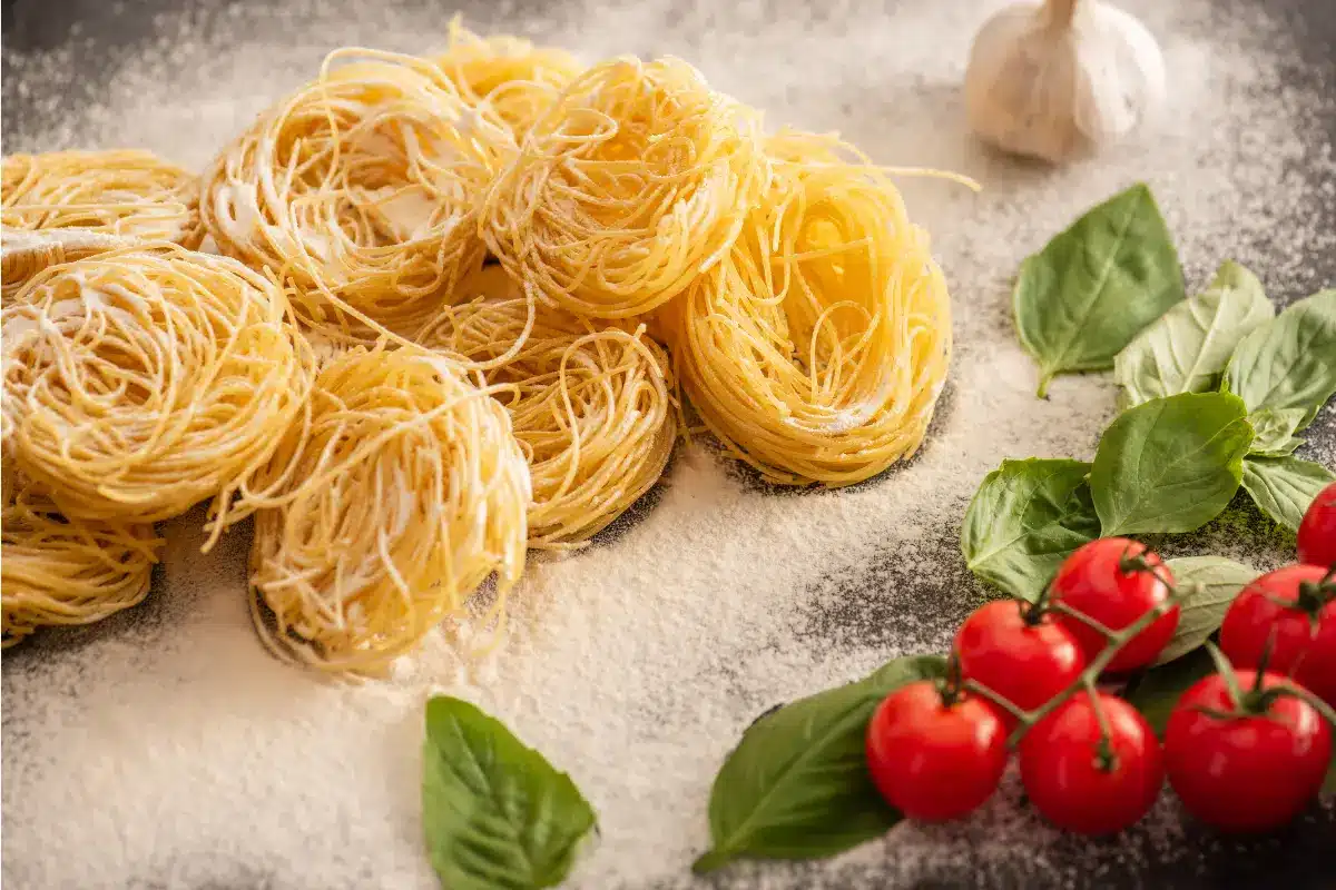 A plate of capellini pasta with garlic, lemon, and Parmesan, garnished with fresh herbs.